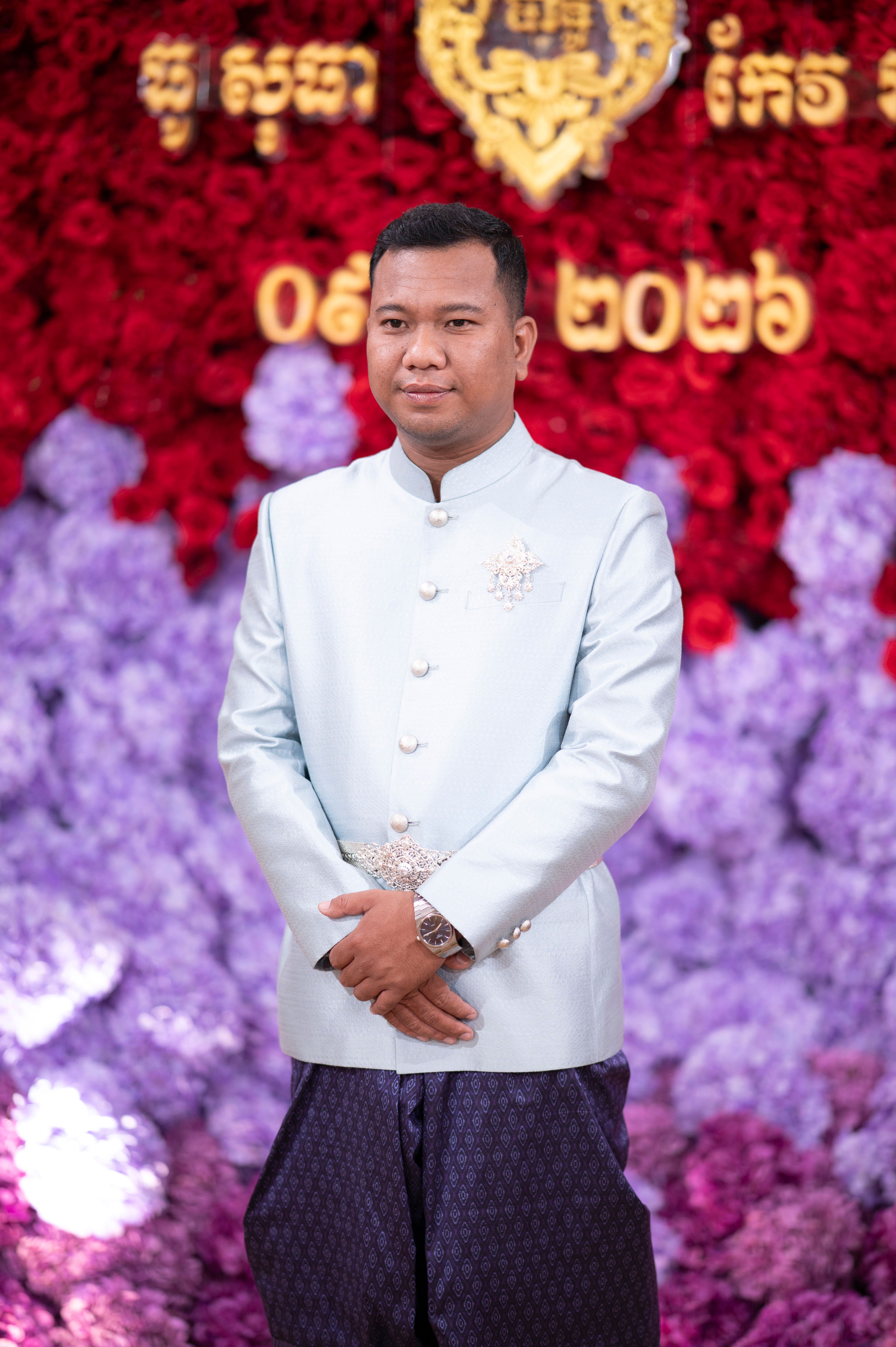 Elegant portrait of a man in traditional Cambodian attire amidst vibrant floral backdrop.