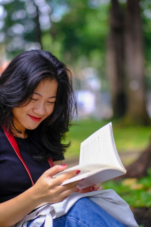 Free A young woman enjoys reading a book outdoors in a Ho Chi Minh City park. Stock Photo