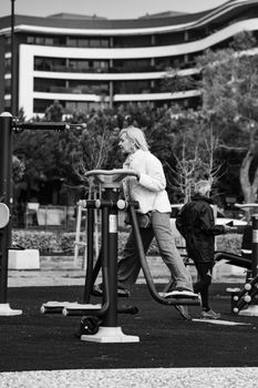 Senior adults exercising on outdoor gym equipment in a city park setting.