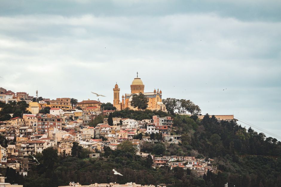 Stunning view of Algiers with Basilica of Notre-Dame d'Afrique overlooking the city under a cloudy sky.