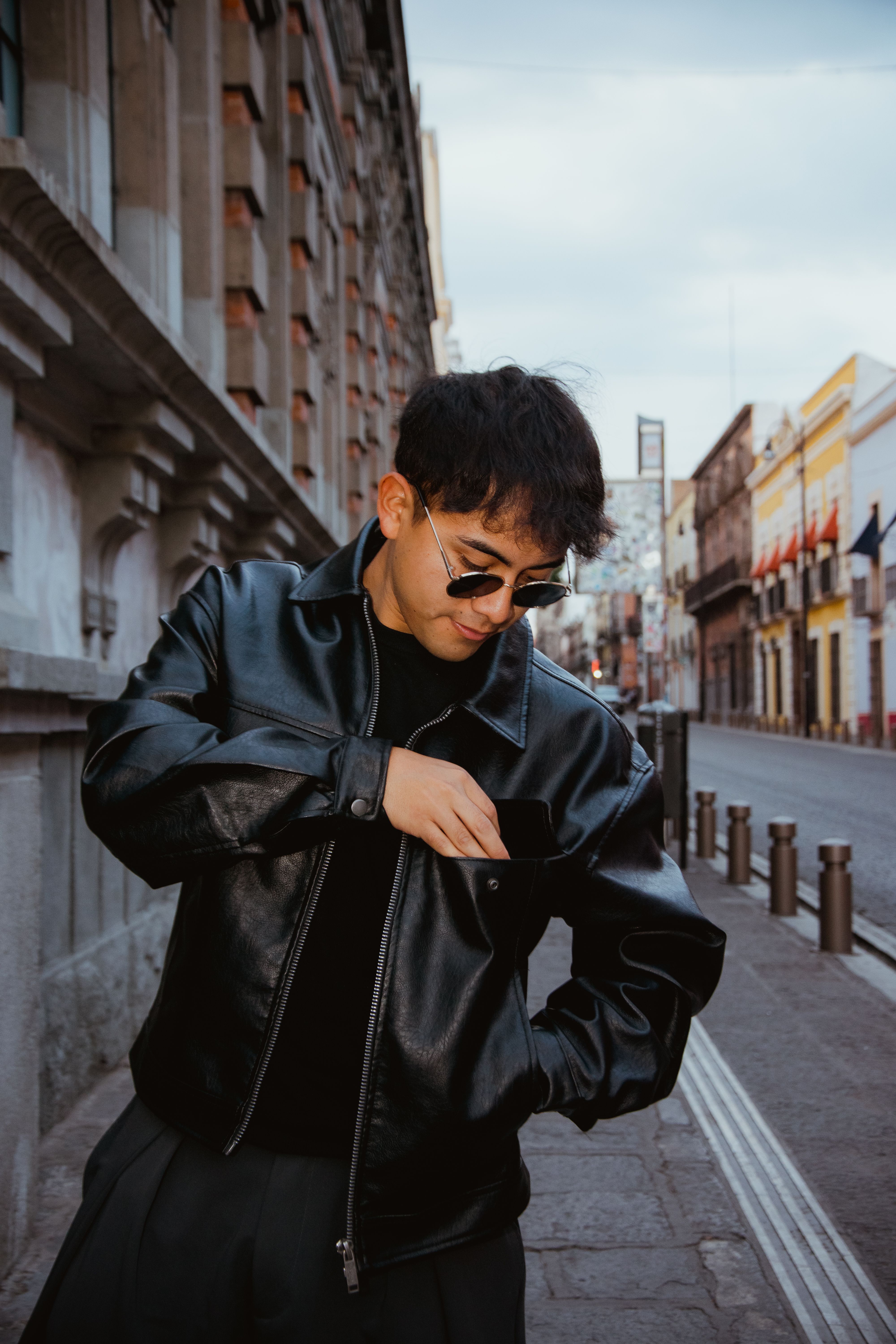 Fashionable man in black leather jacket and sunglasses standing on urban street in Puebla, Mexico.