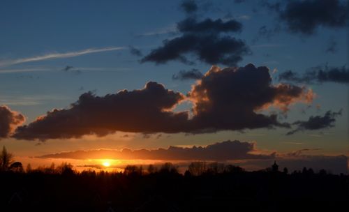 Free Silhouetted trees and rooftops under a vibrant sunset with dramatic clouds. Stock Photo