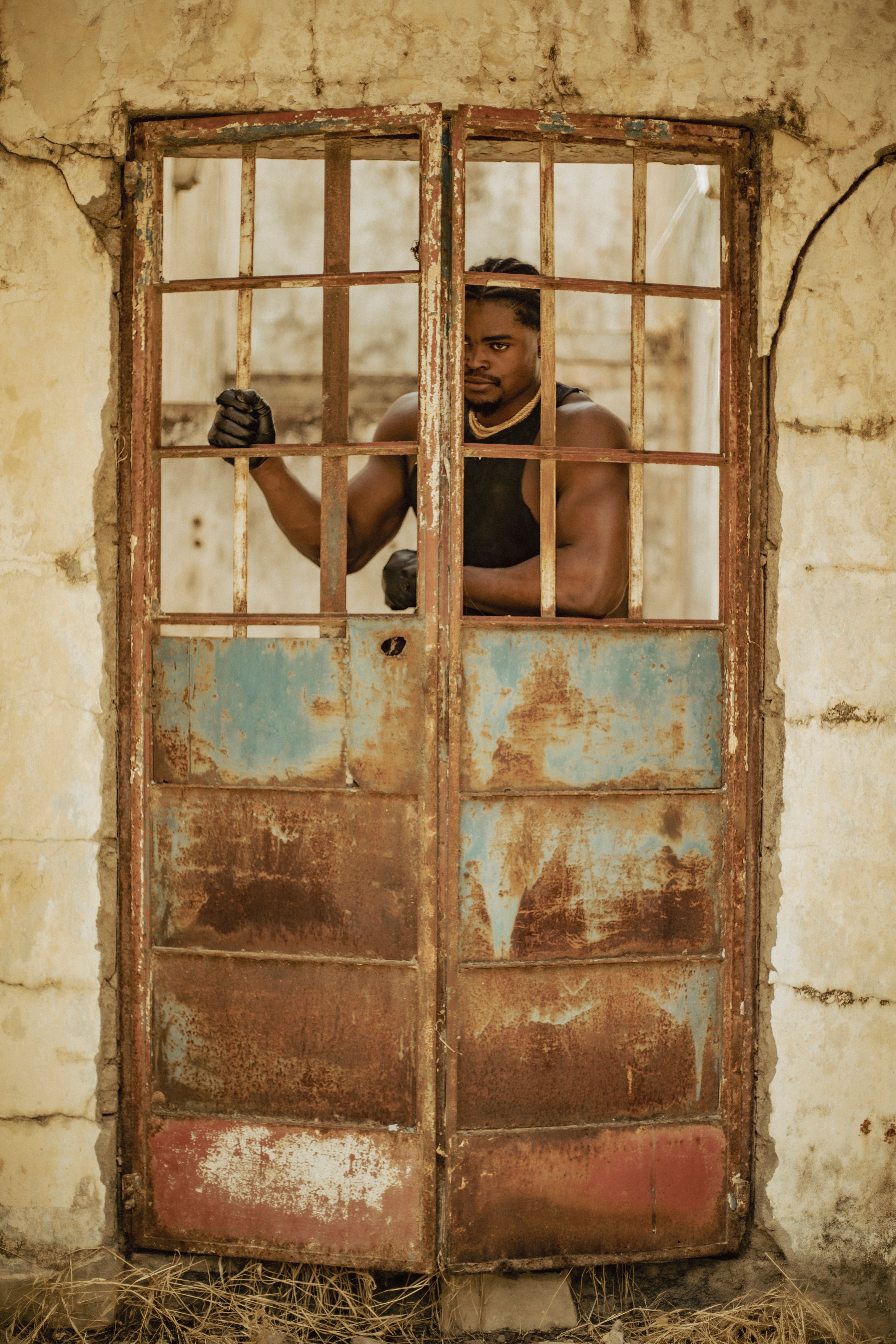 Confident man standing behind a rustic metal door in an abandoned setting, expressing resilience.