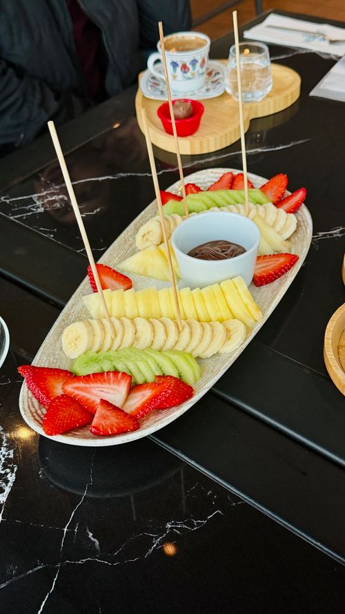 Free A vibrant fruit platter with strawberries, bananas, and kiwis served with chocolate dip on a marble table. Stock Photo