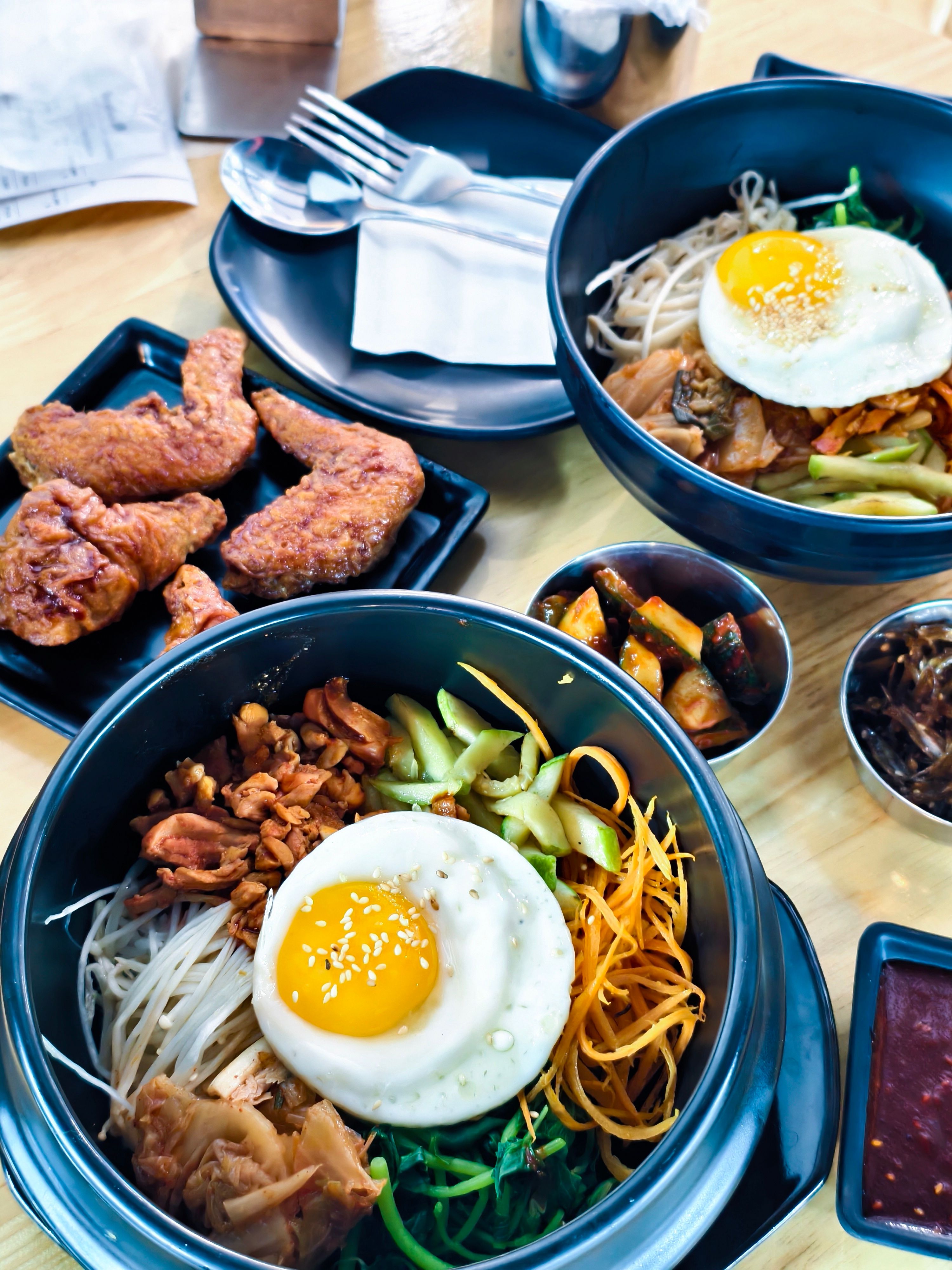 Top-down view of Korean bibimbap bowls and crispy fried chicken with side dishes on a wooden table.