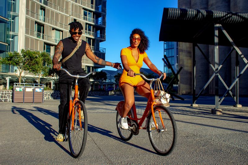 Happy couple biking outdoors in a city, enjoying a sunny day on orange bicycles.