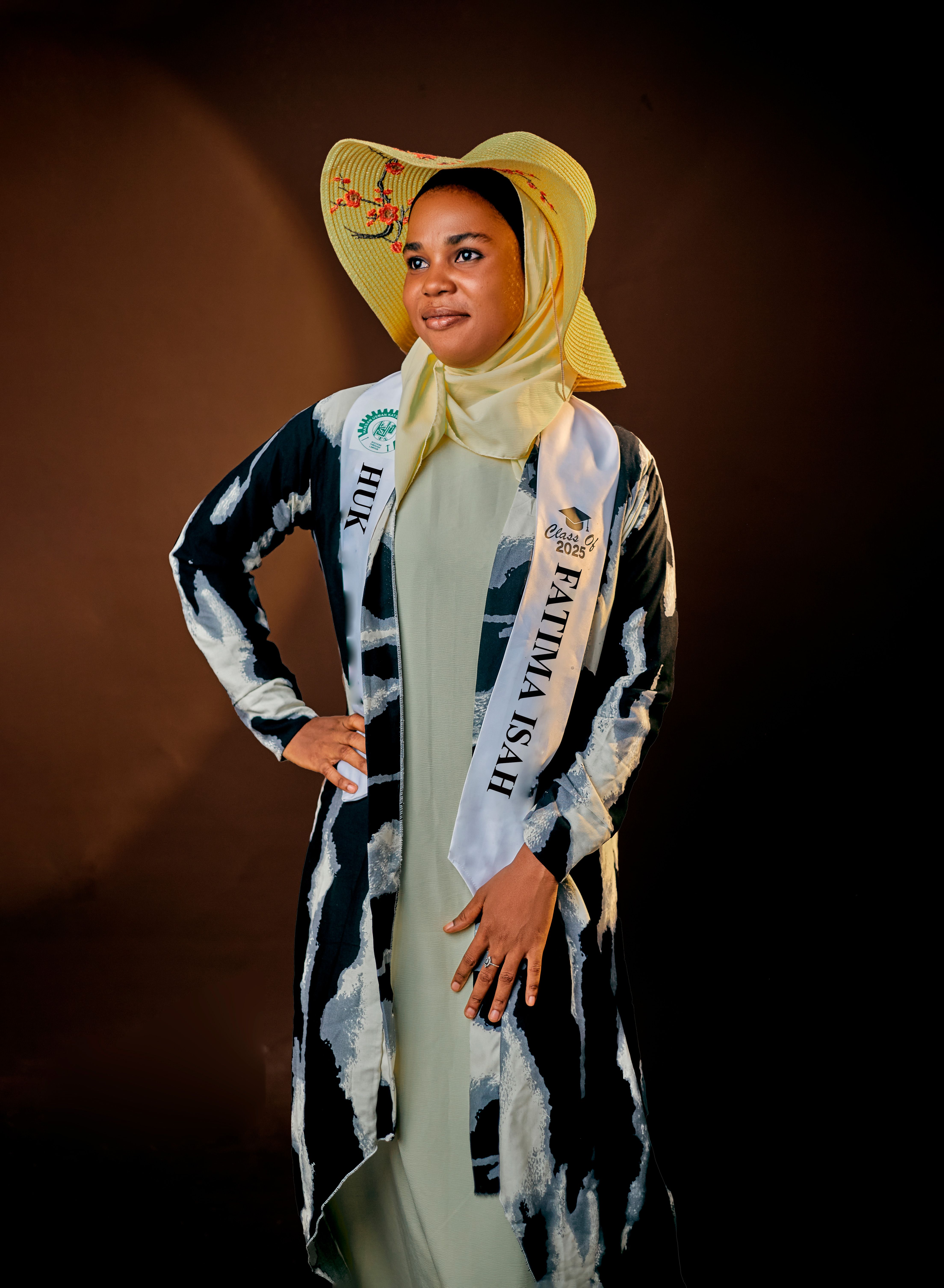 Portrait of a woman wearing a stylish hijab and hat against a dark background.