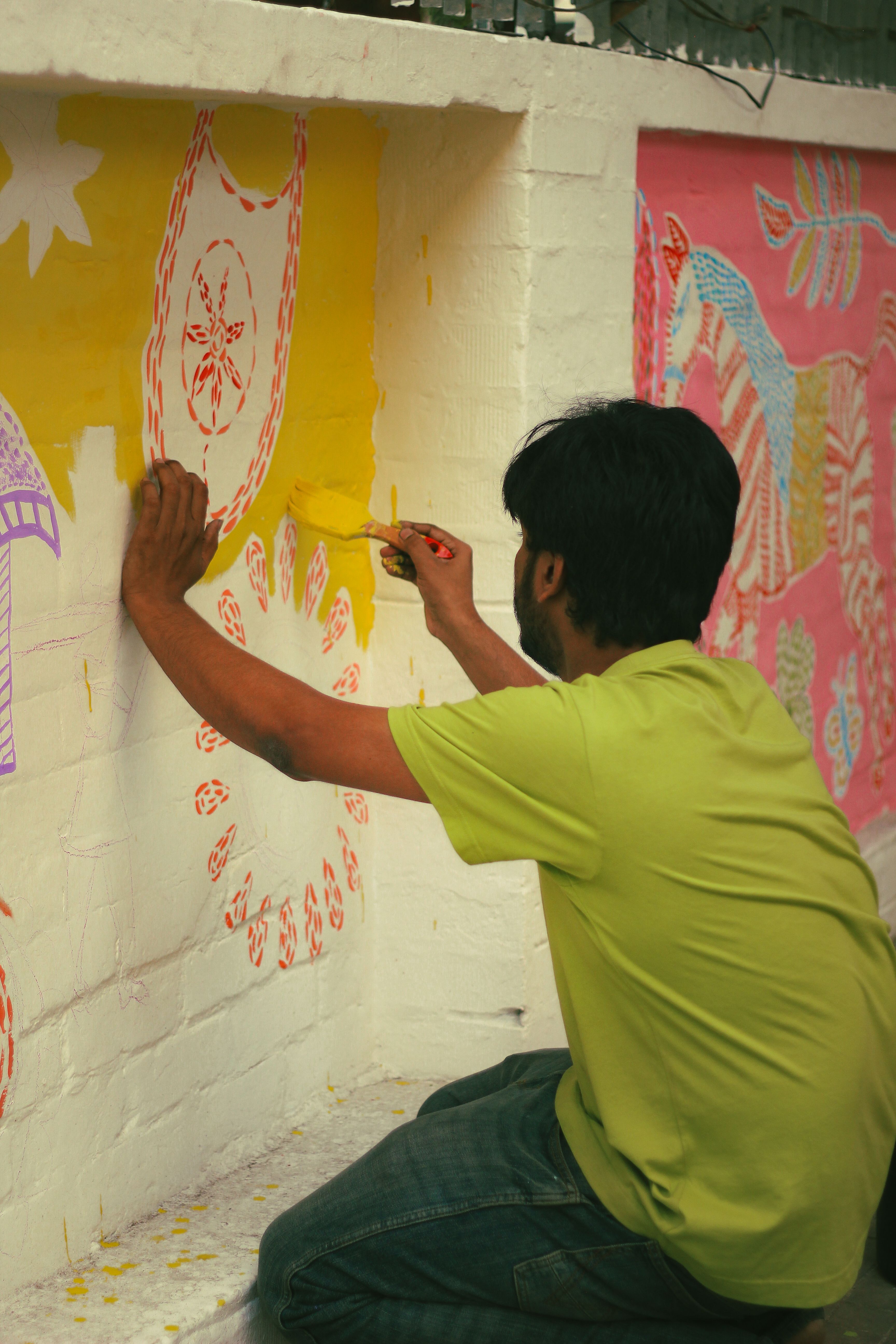 A man creating colorful street art on a wall in Dhaka, capturing the vibrant local culture.