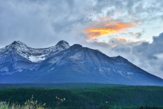 Stunning view of a snow-capped mountain in Banff, Alberta with dramatic sky at sunset.