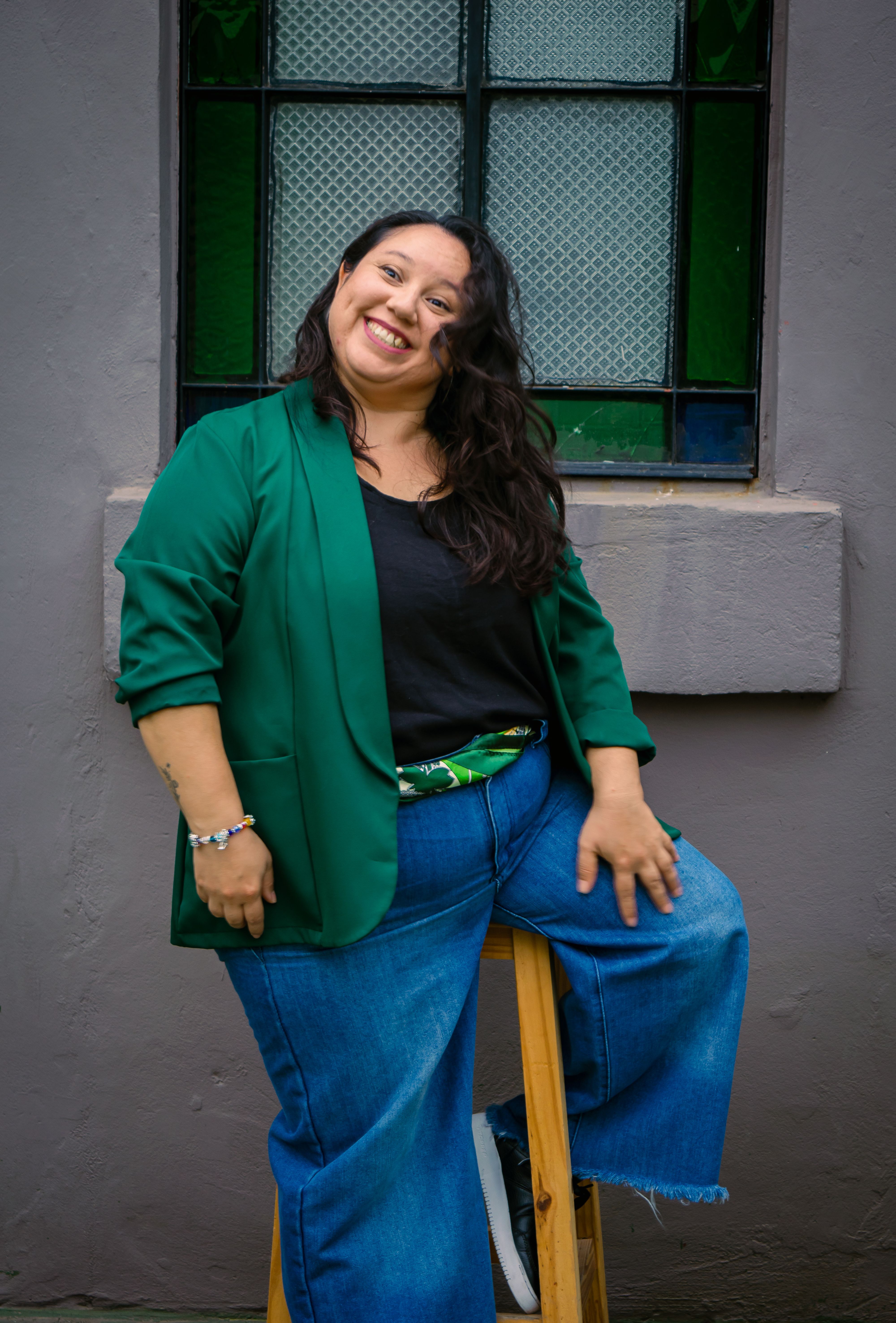 Cheerful woman in casual attire sits by a stained glass window, exuding confidence and warmth.