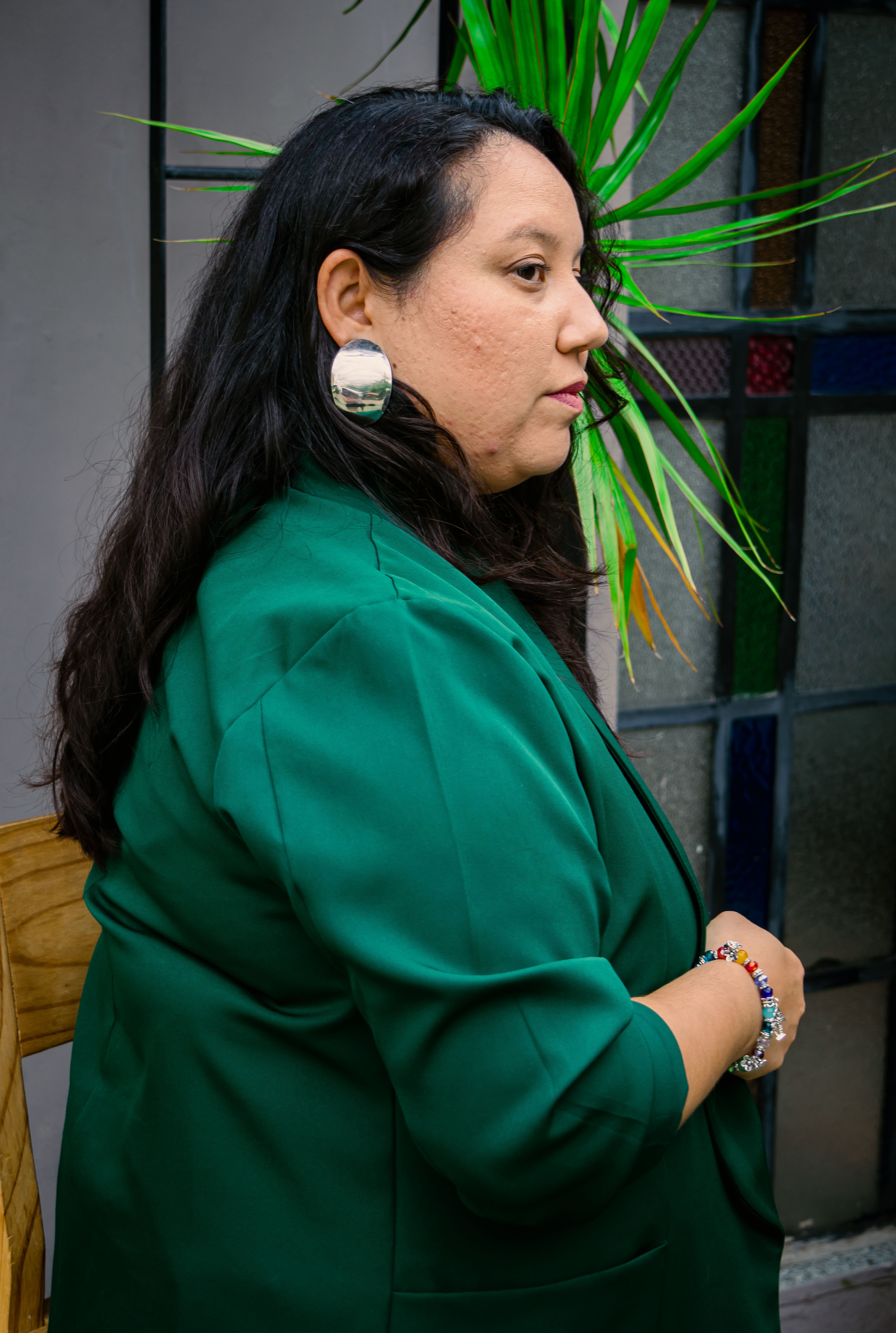 Side profile of a woman in a green blazer with a silver earring, indoors.