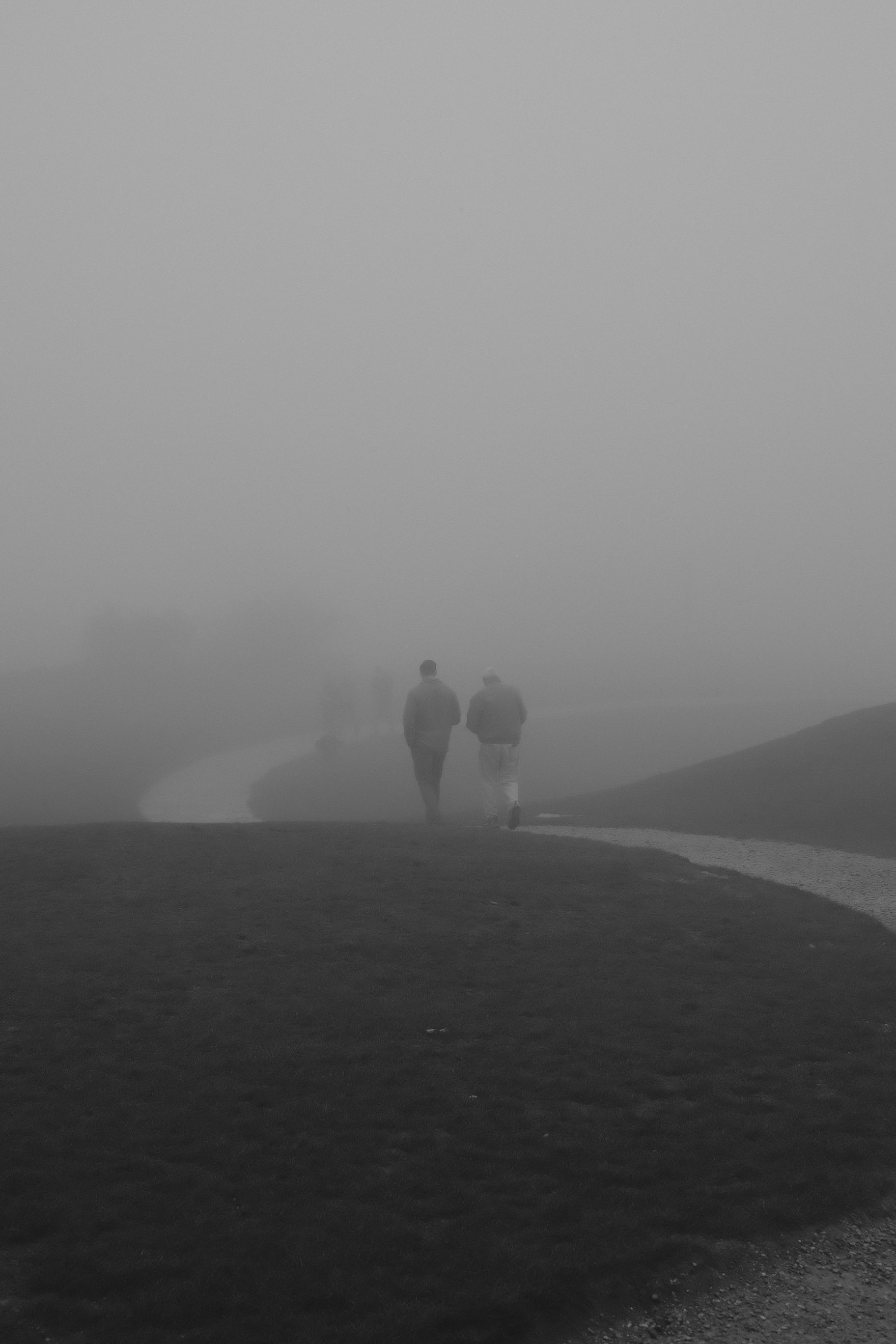 Two people walking on a foggy path in England, creating a mysterious ambiance.