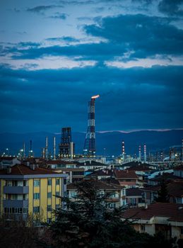Evening view of a city with industrial smokestacks under a cloudy sky, showcasing urban-industrial contrast.