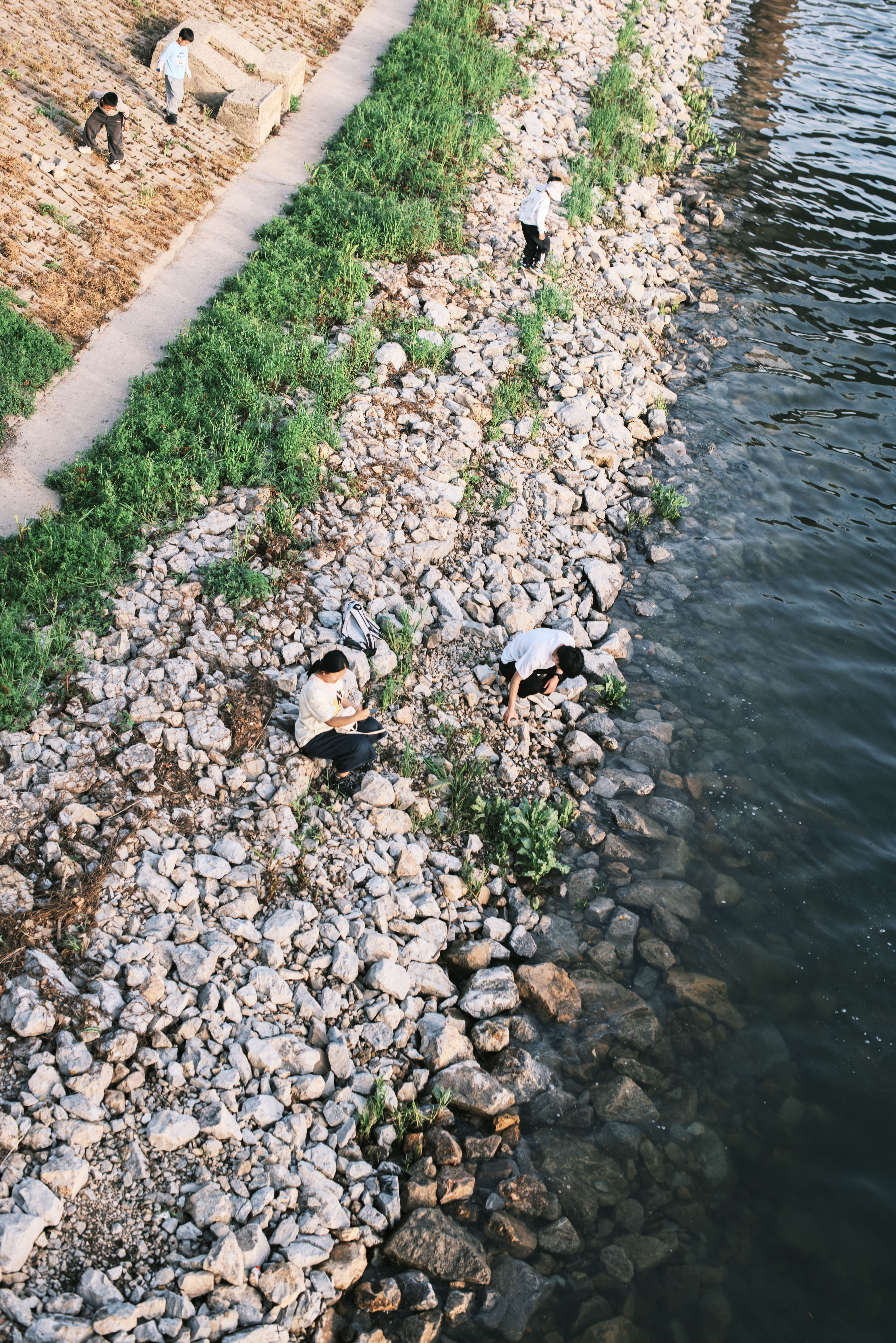 People Relaxing by Riverside Pebble Path · Free Stock Photo