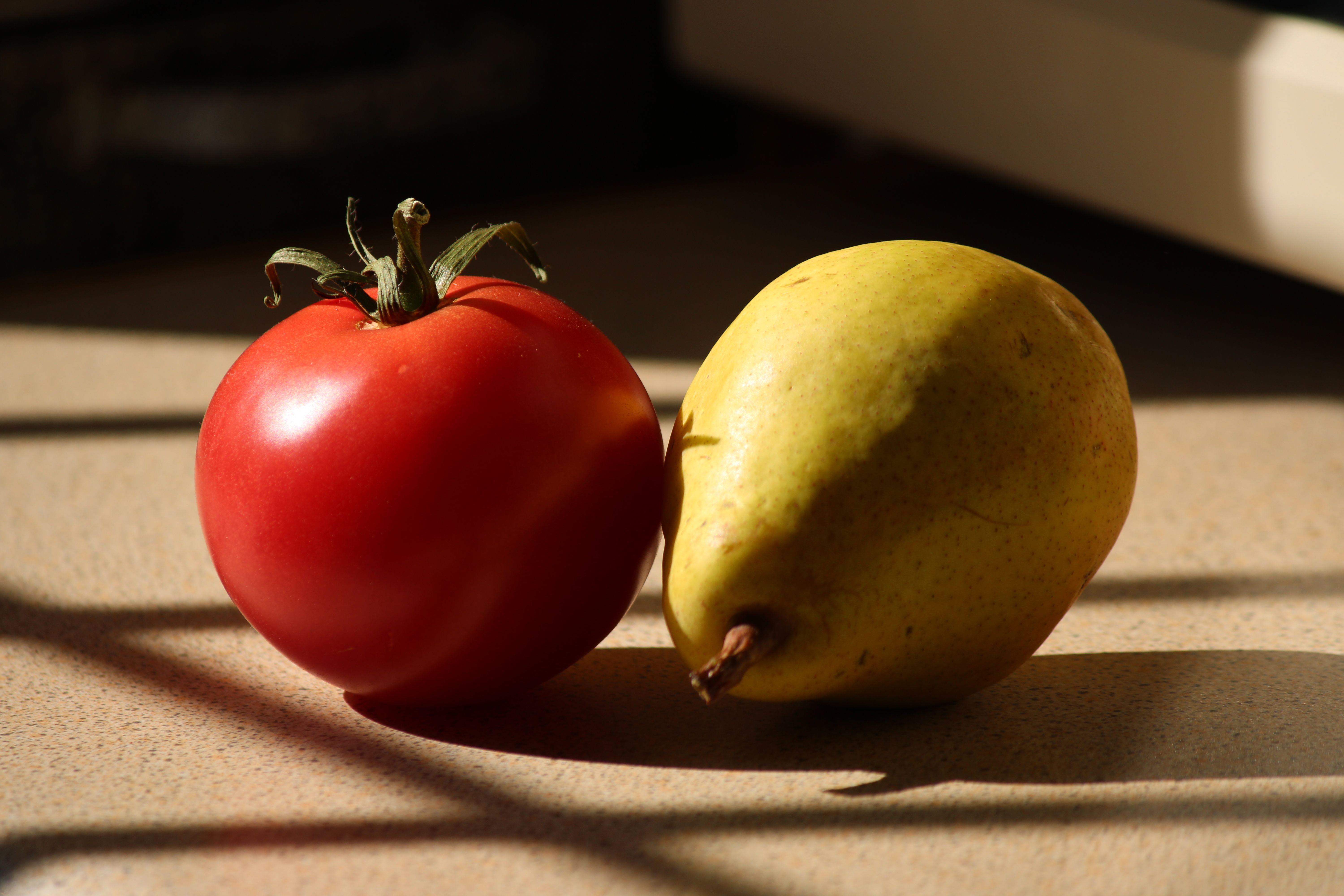 A ripe tomato and a pear bathed in sunlight on a kitchen counter. Vibrant and fresh.