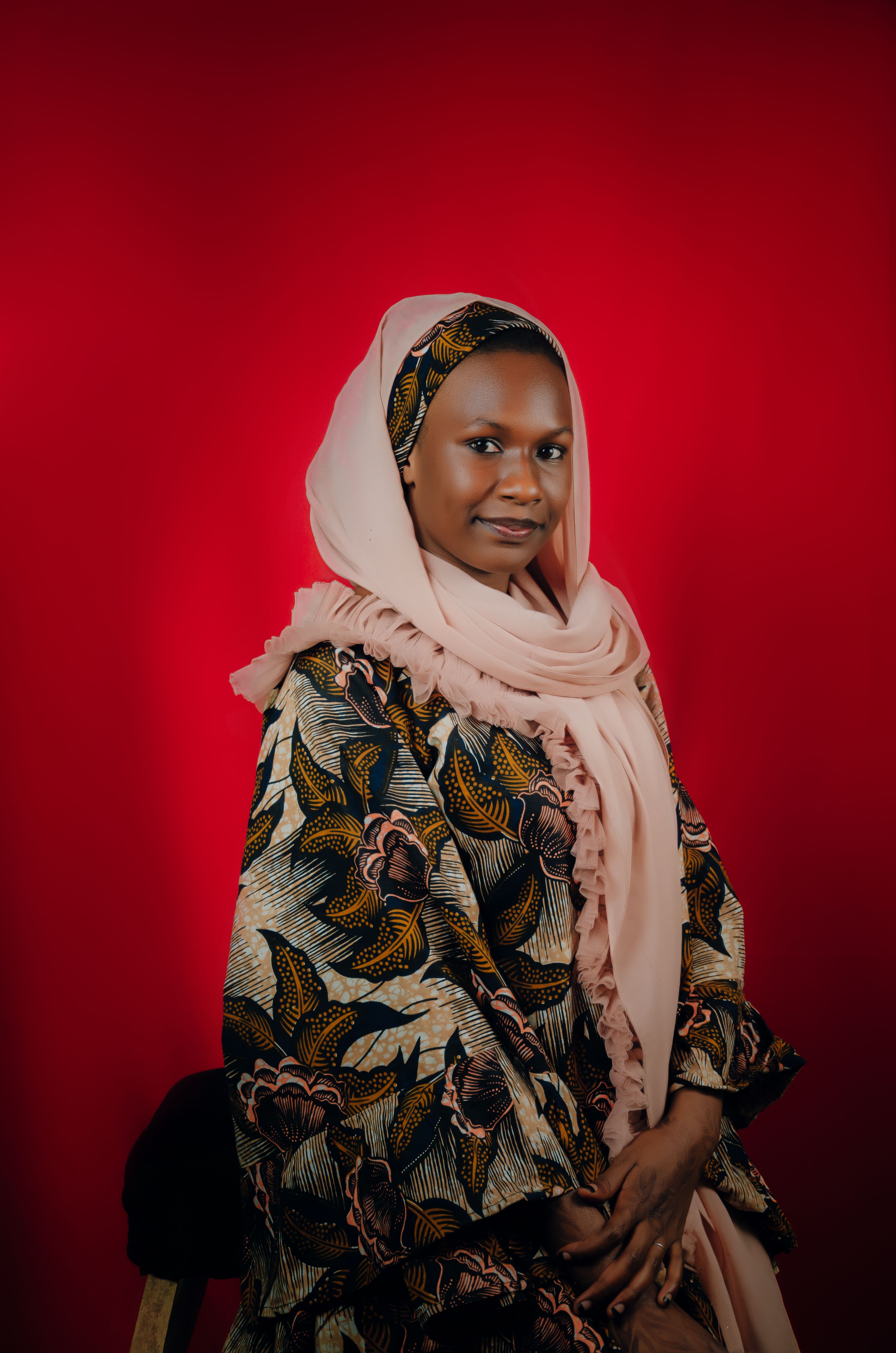 Portrait of a woman in colorful traditional attire and headscarf against a vibrant red background.