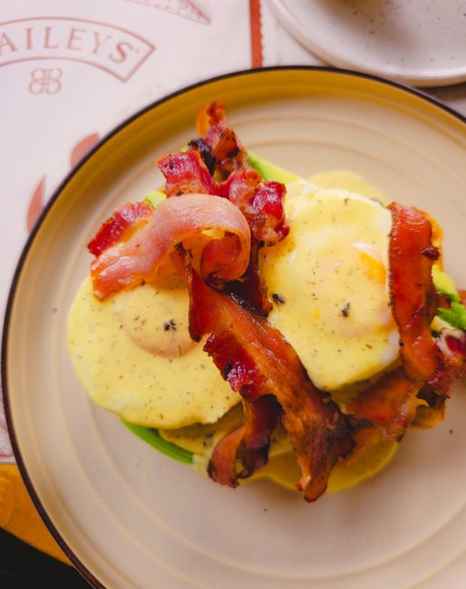 A golden baked egg casserole in a glass baking dish, studded with bacon pieces, melted cheddar, and diced red peppers, cut into squares.
