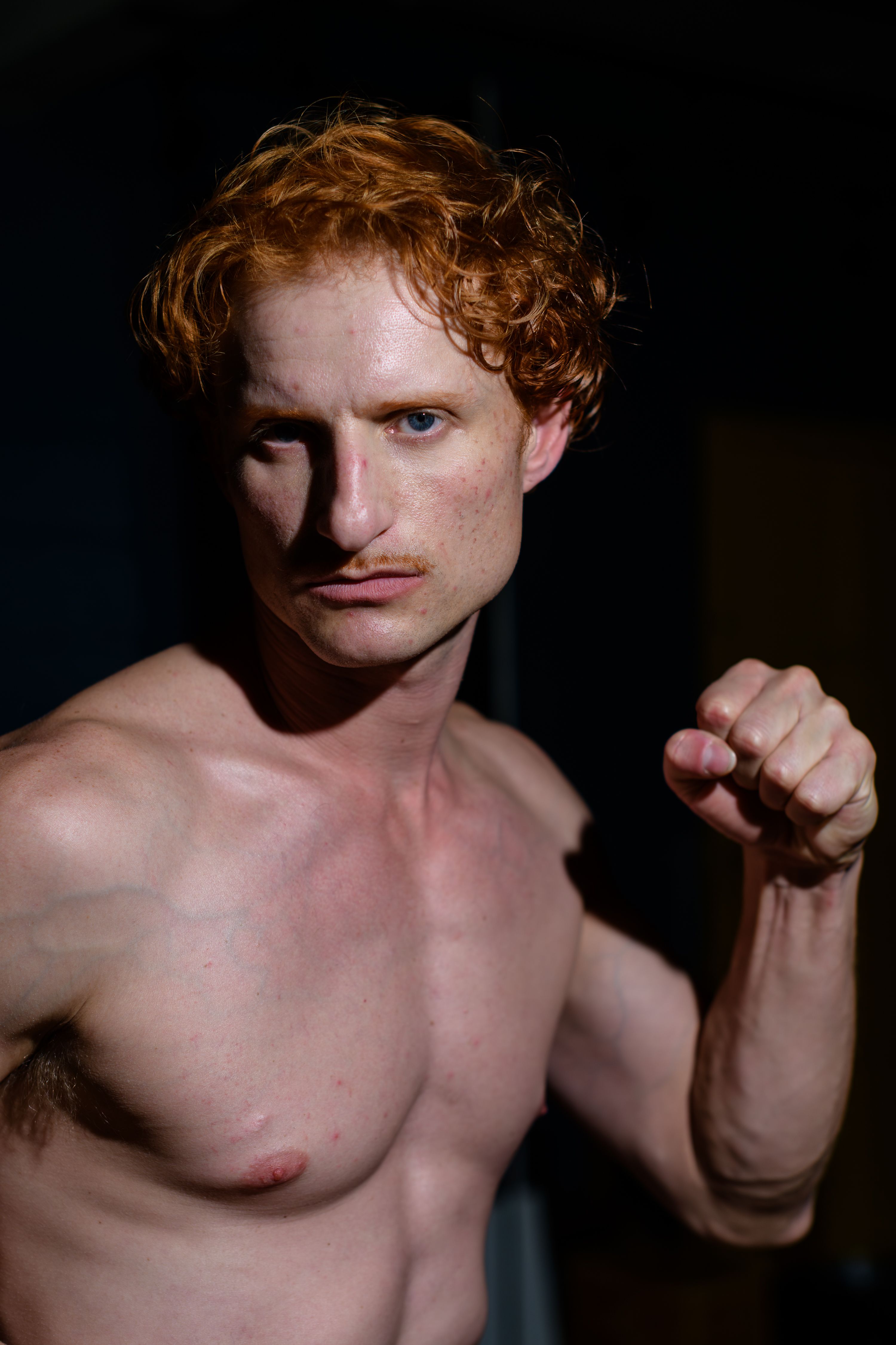 Close-up portrait of a red-haired male model with a serious expression and dynamic pose.