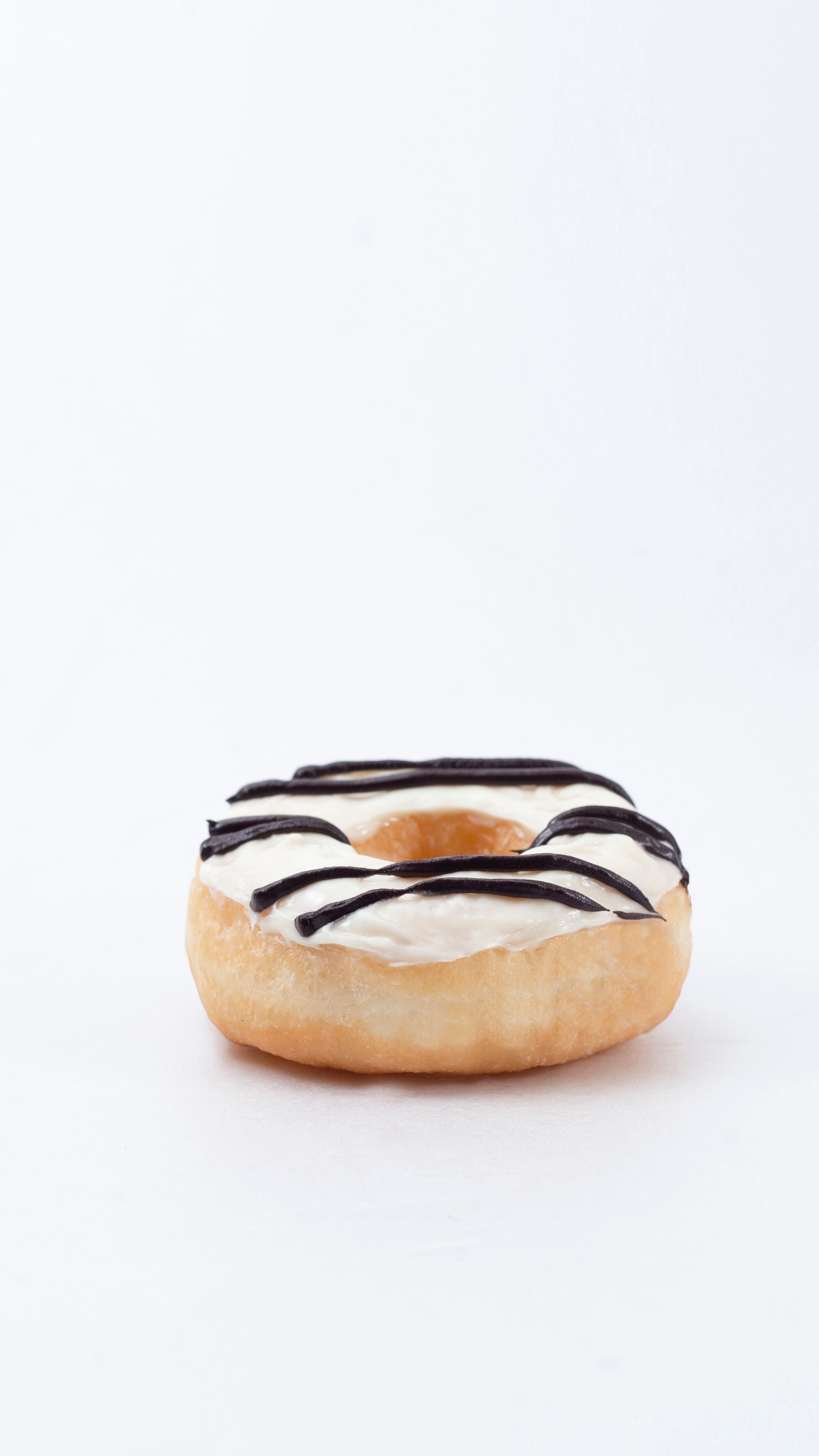 Tasty vanilla donut topped with chocolate drizzle on white background.