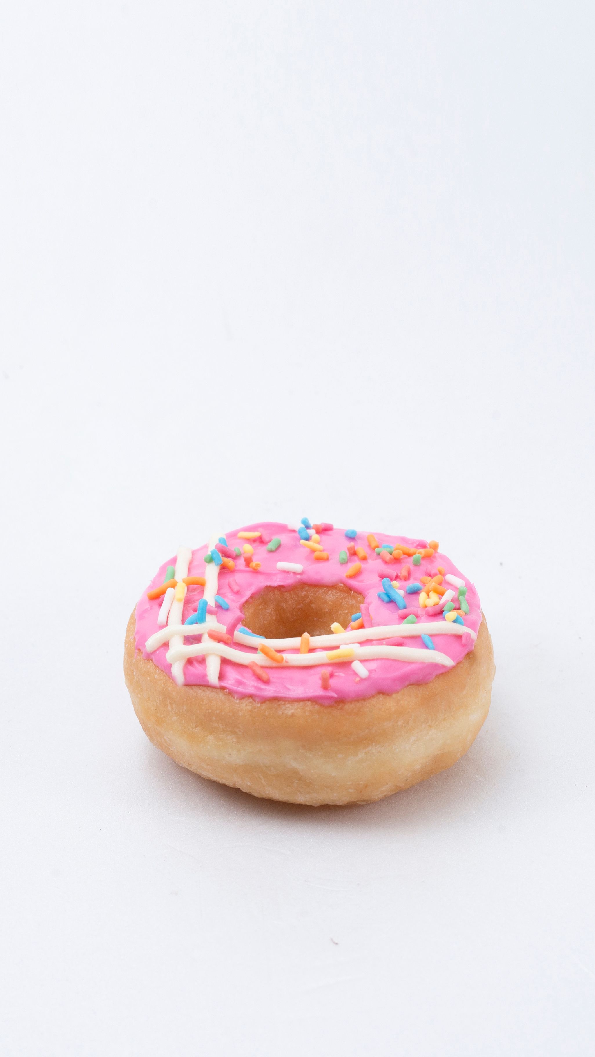 Close-up of a pink frosted donut with colorful sprinkles isolated on a white background.