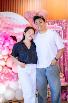 Happy couple posing at a vibrant pink-themed birthday party with balloons.