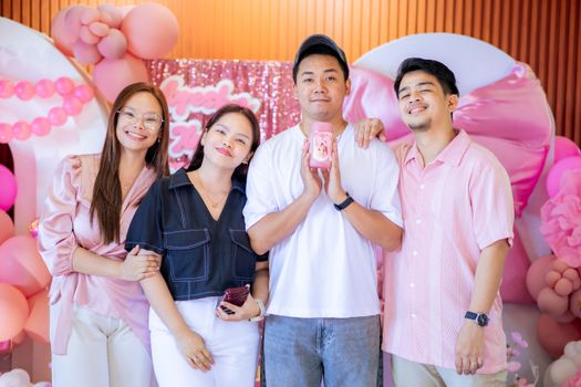 A group of friends celebrating indoors with balloons and decorations in pastel colors.