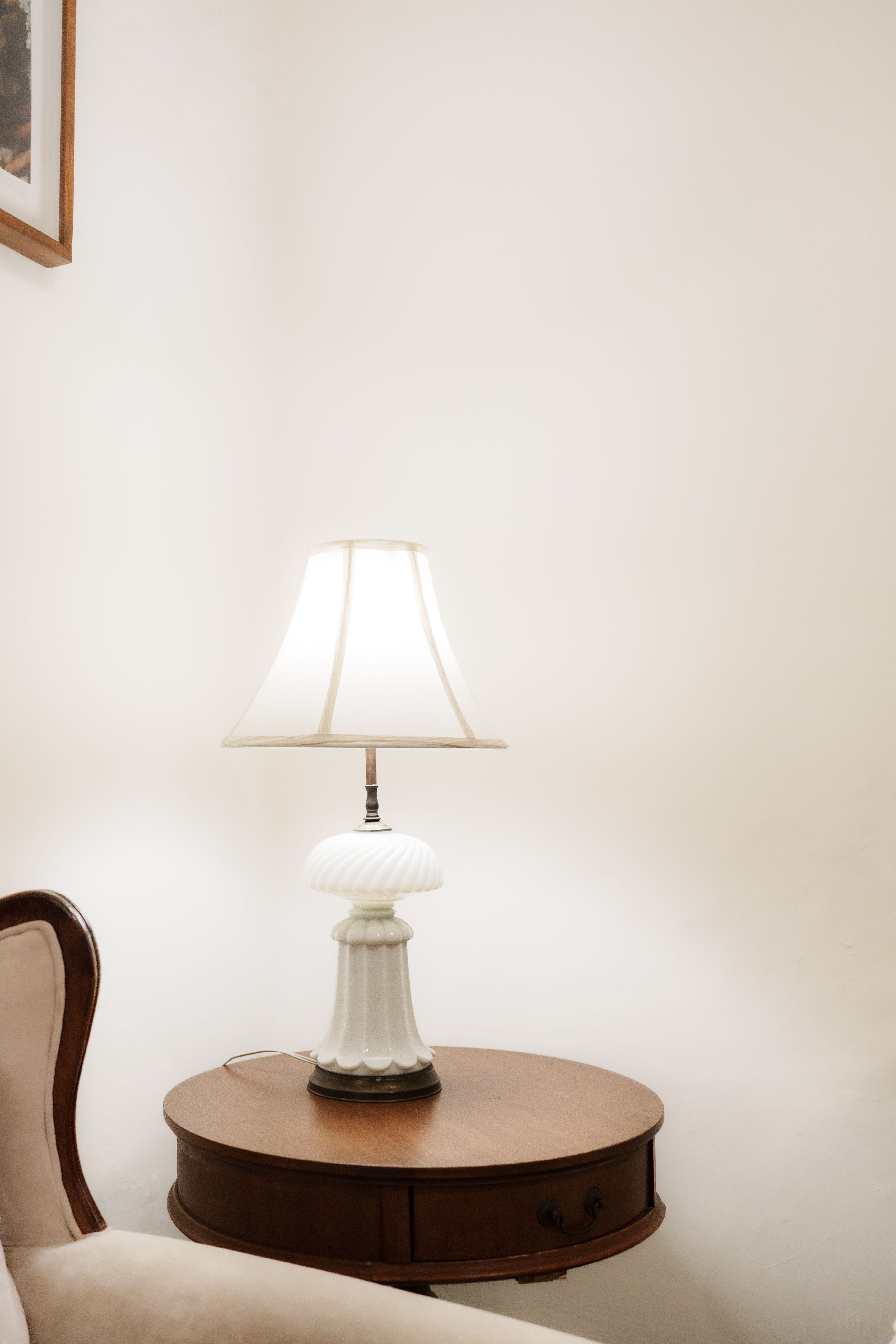Warmly lit bedroom scene featuring a classic white lamp on a round wooden table.