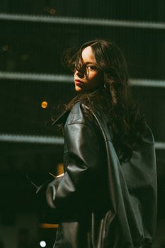 Young woman with leather jacket turning at night, urban setting.