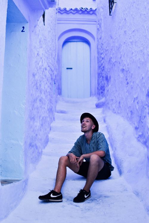 Free A man in casual attire relaxes in the blue alleys of Chefchaouen, capturing the town's unique charm. Stock Photo