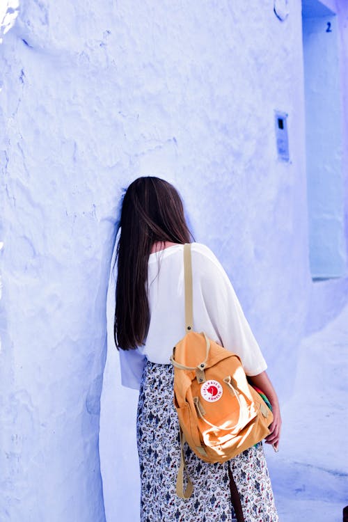 Woman in White Shirt Leaning on Blue Concrete Wall