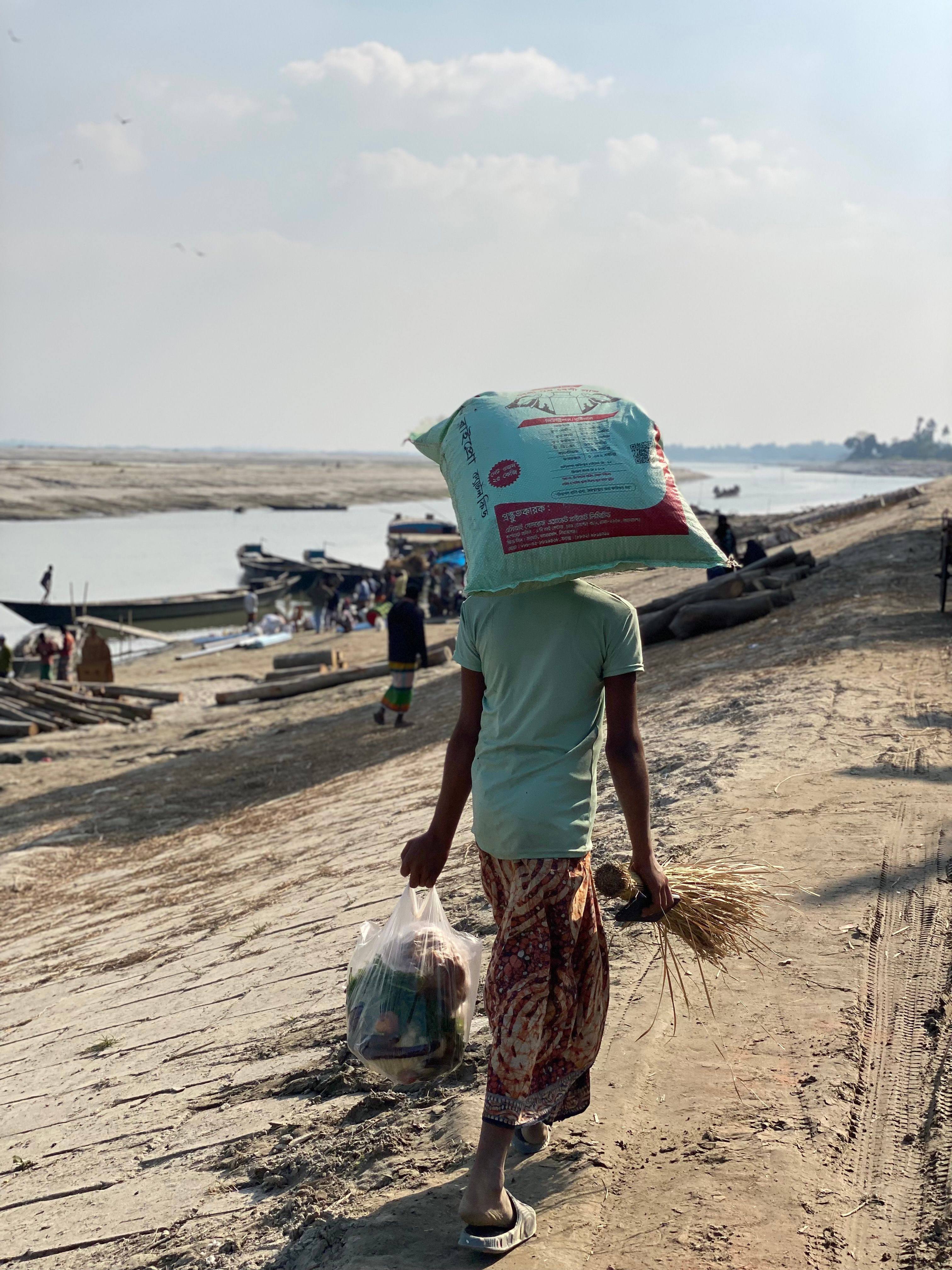 Child carrying rice bag along riverbank · Free Stock Photo