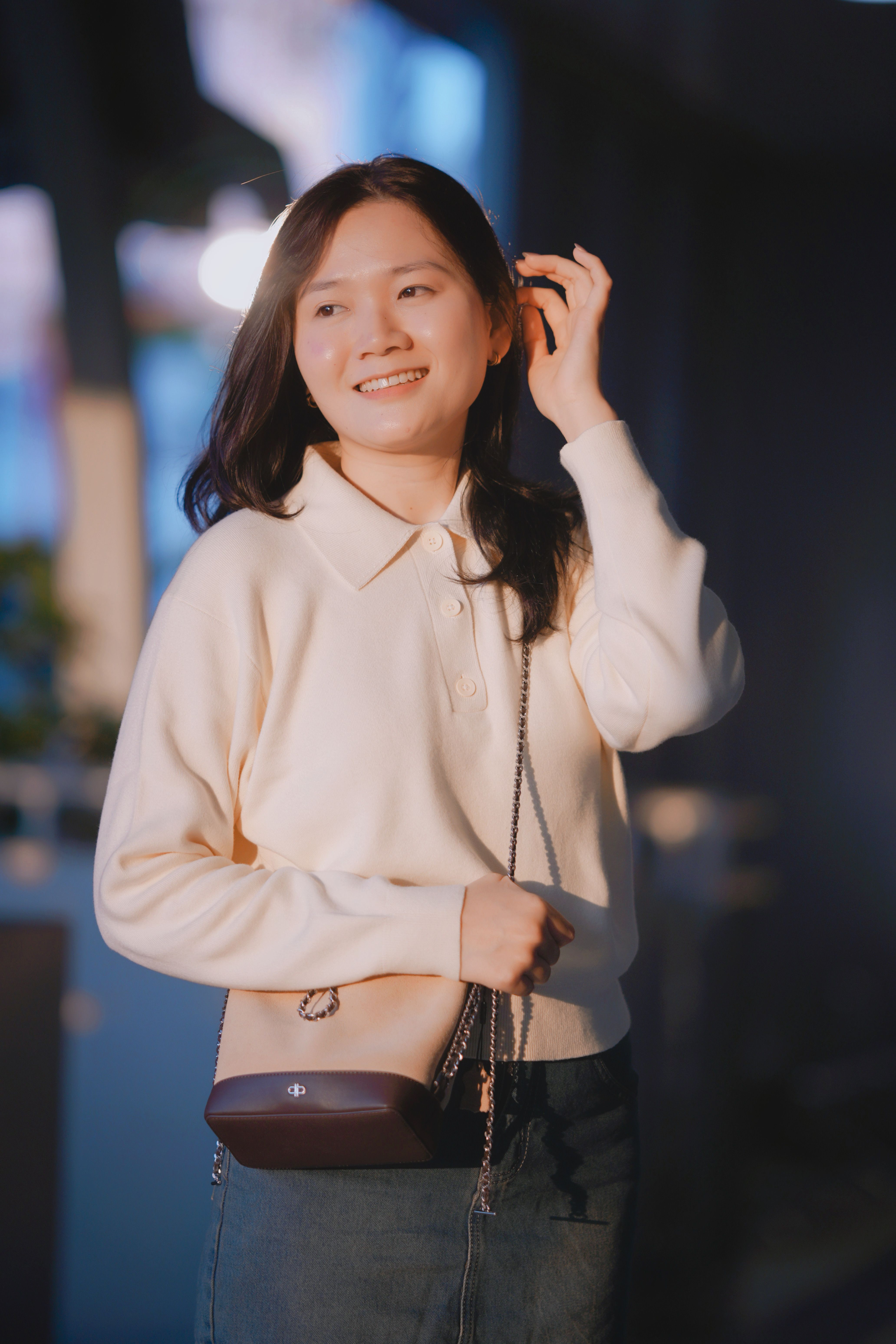A young woman in casual attire looking content outdoors during the day.