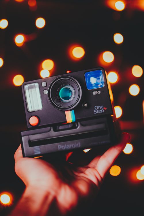 Free Hand holding a classic Polaroid camera with glowing bokeh lights in the background, creating a nostalgic mood. Stock Photo