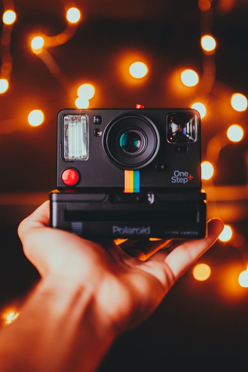 Free Close-up of a vintage Polaroid camera held against a warm bokeh background. Stock Photo