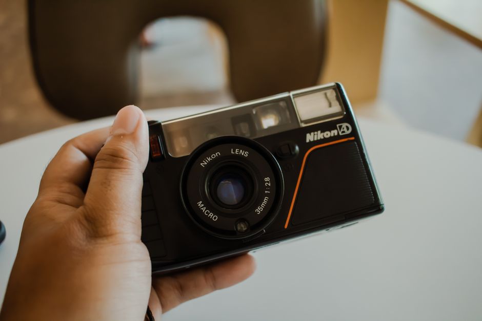Fotógrafo segurando câmera compacta analógica com objetiva 35mm em calçada movimentada