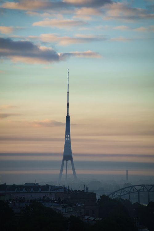 Free Scenic view of the Riga TV Tower amidst morning mist and vibrant sky, capturing the essence of Latvia's skyline at dawn. Stock Photo