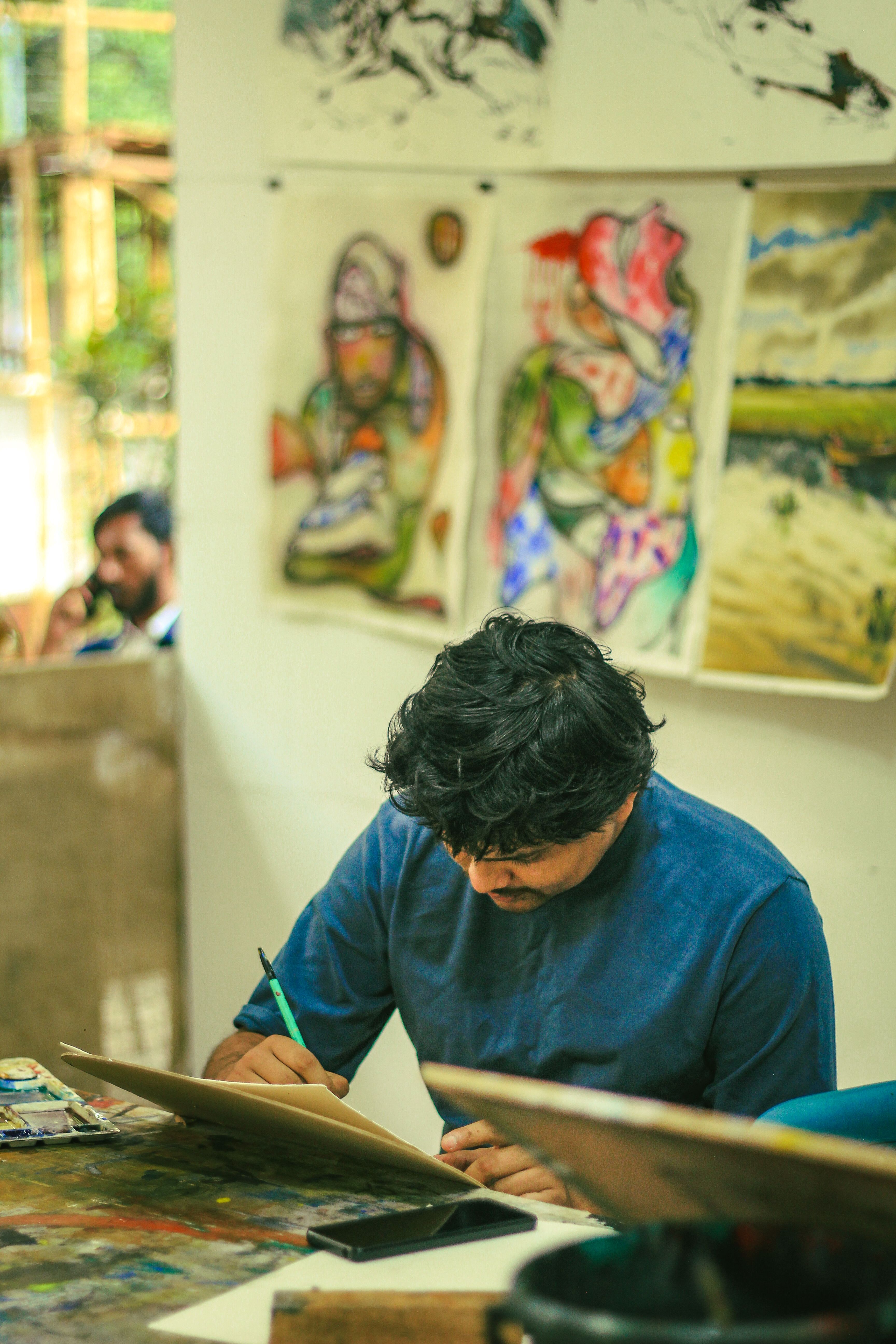 An artist engaged in sketching at a vibrant studio in Dhaka, surrounded by colorful artwork.