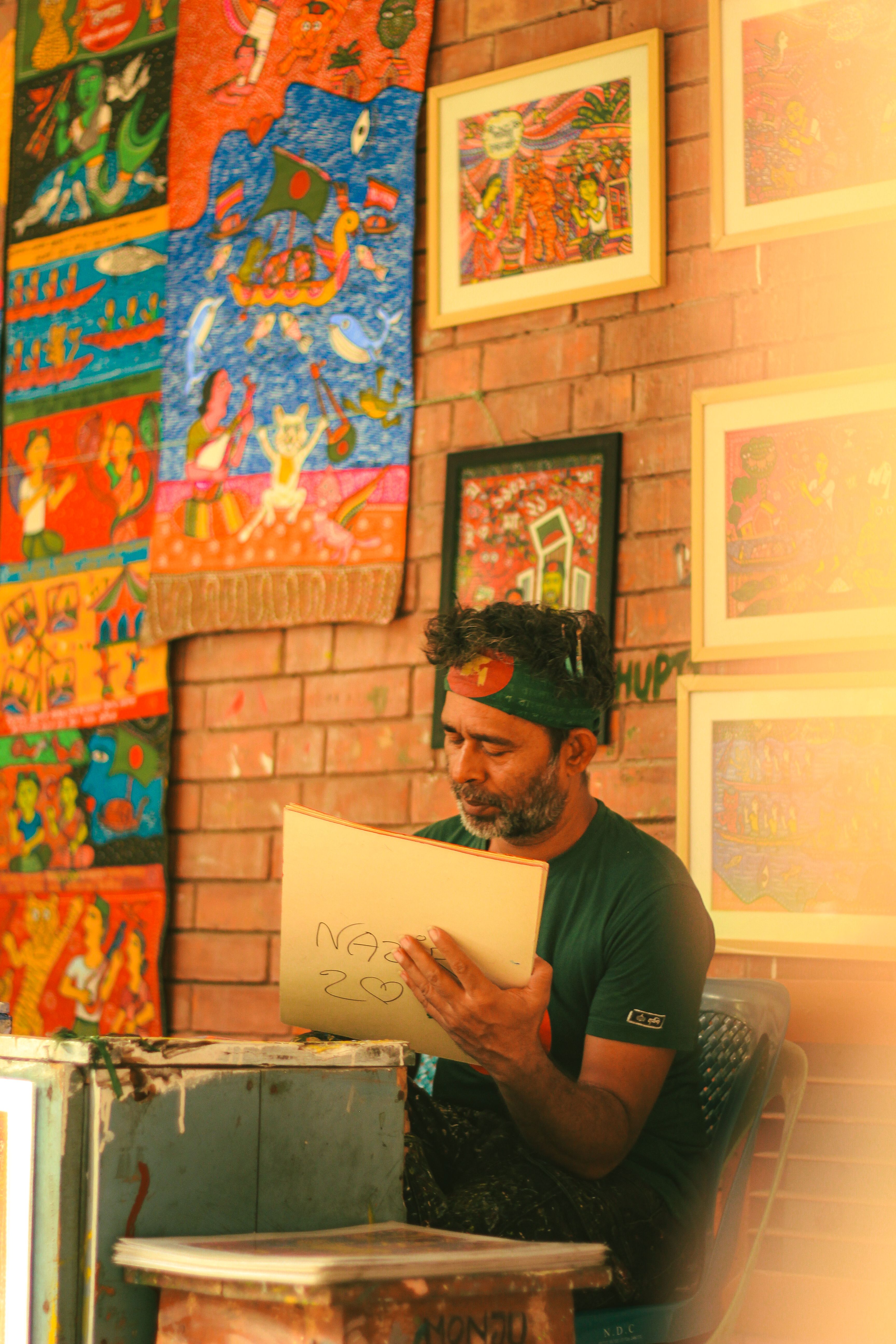 A South Asian artist engrossed in creating art inside a colorful Dhaka gallery.