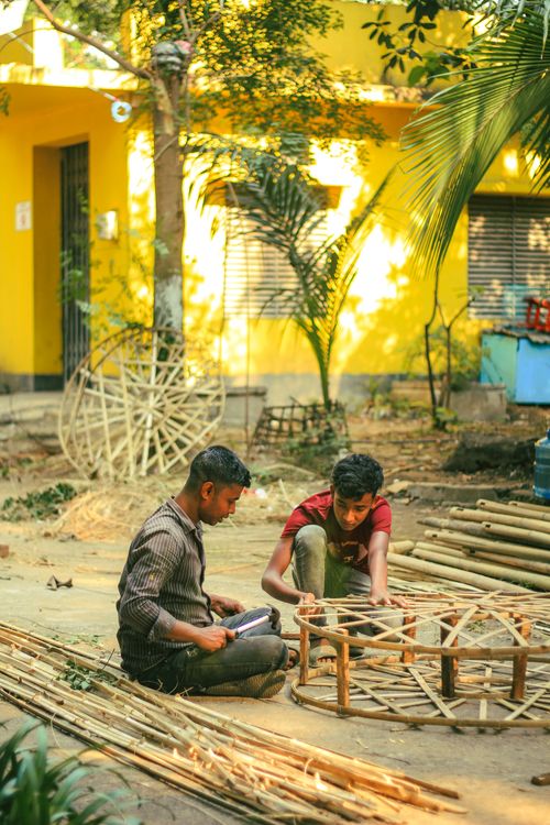 Free Two craftsmen working on bamboo art outside a colorful building in Dhaka, Bangladesh. Stock Photo