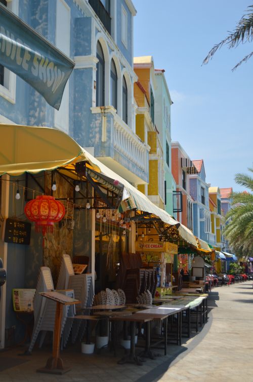 Free A lively street with colorful buildings and cafe tables under bright summer skies, exuding a vibrant atmosphere. Stock Photo