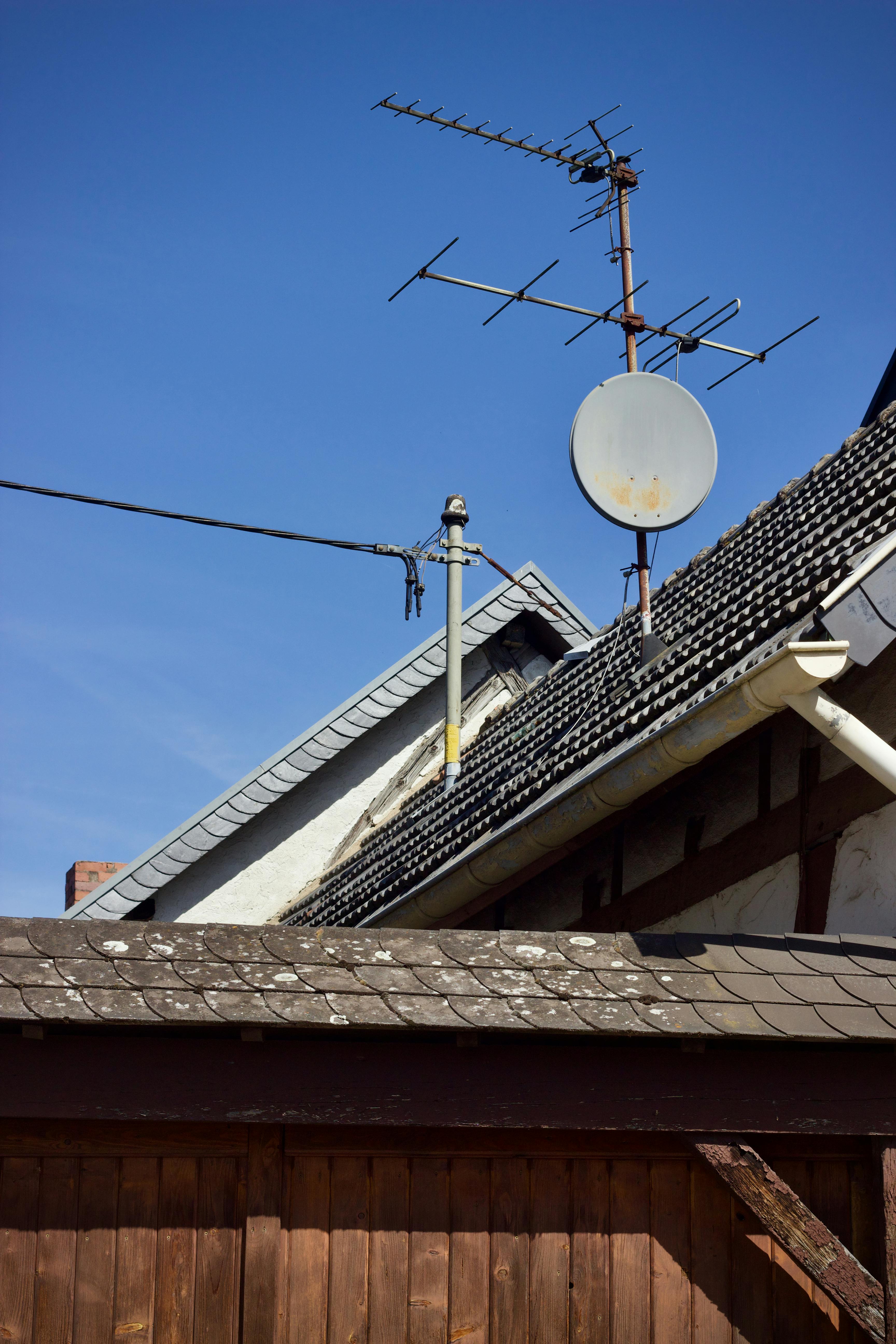 A rooftop with an antenna and satellite dish on a traditional styled house.