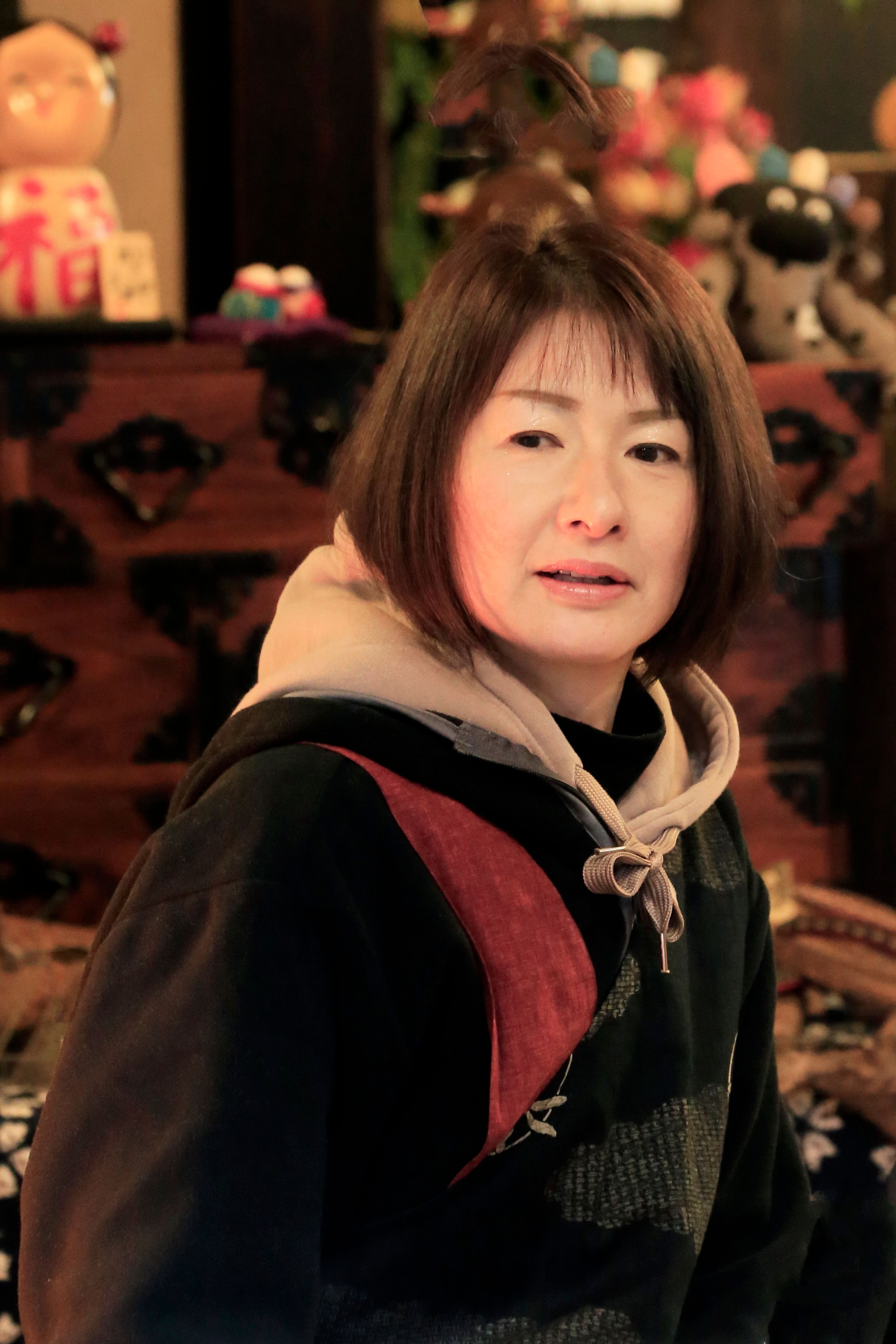 A woman in a hoodie indoors with Japanese decor creates a warm, inviting atmosphere.
