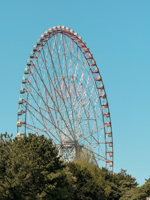 Free A stunning view of a giant Ferris wheel in Tokyo, Japan, framed by lush green trees under a clear blue sky. Stock Photo