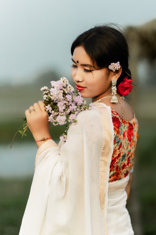 Free A graceful Bangladeshi woman holding flowers, with traditional attire and jewelry, captured outdoors. Stock Photo