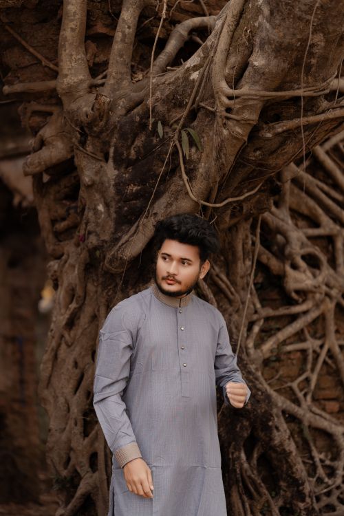Free A young man wearing traditional Panjabi clothing stands confidently by a large tree in Bangladesh. Stock Photo