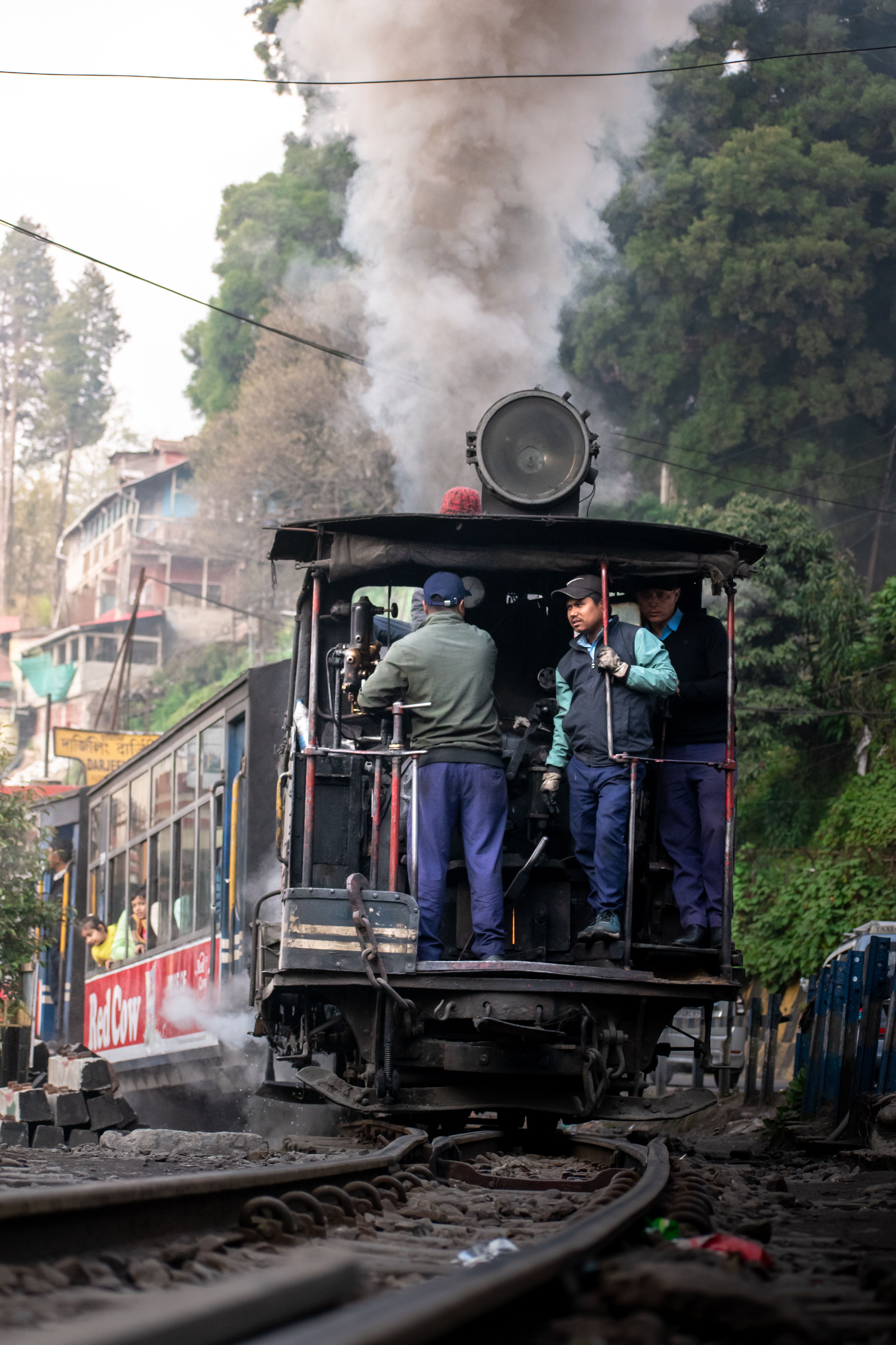 Crew riding the front of a Darjeeling Himalayan Railway steam engine as it pulls away in a cloud of smoke