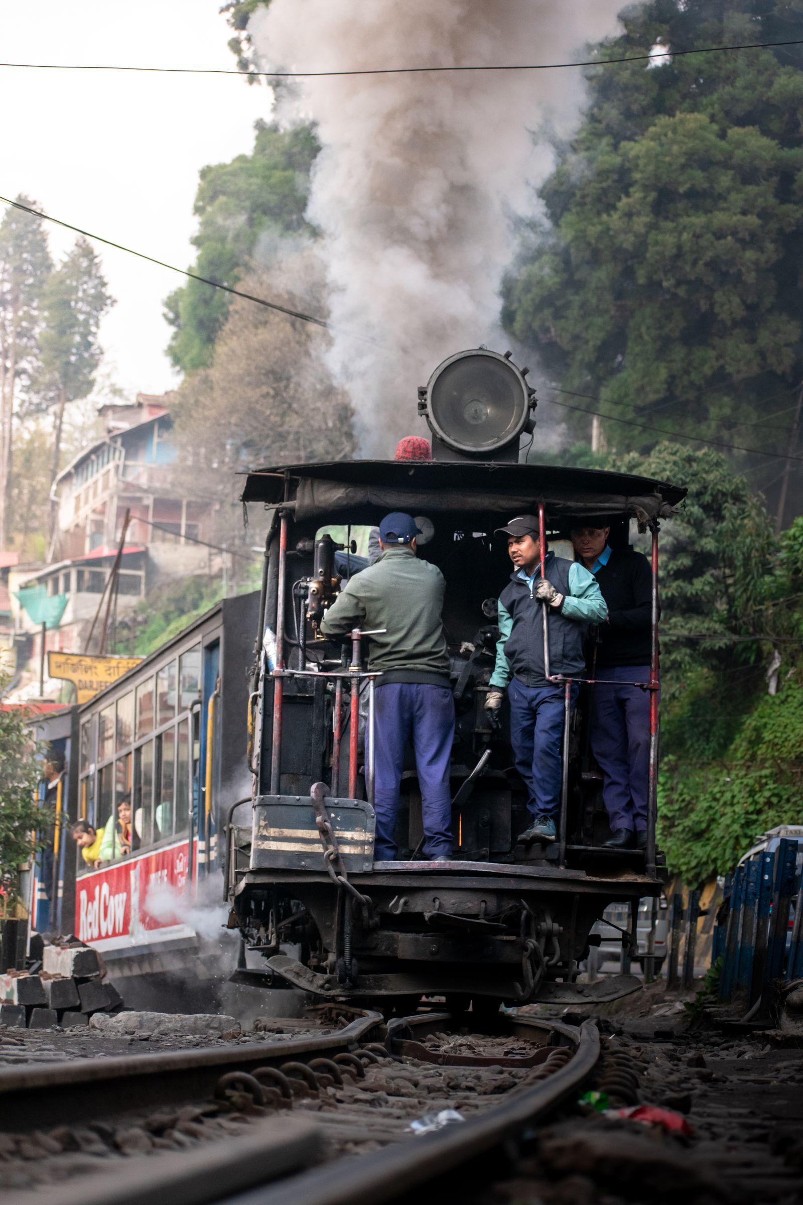 Crew riding the front of a Darjeeling Himalayan Railway steam engine as it pulls away in a cloud of smoke