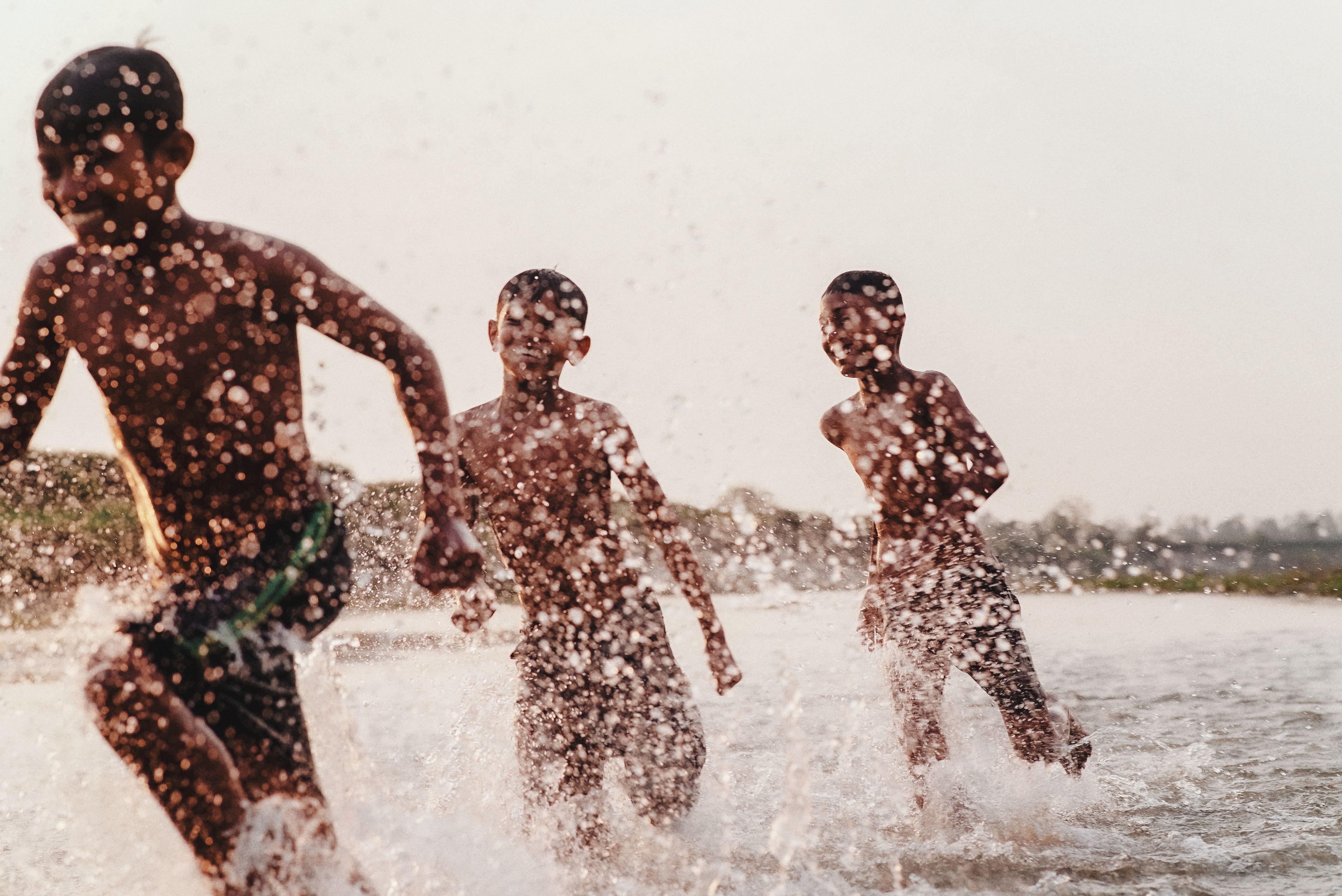 Three children splash energetically in a river, capturing the essence of joyful summer play.