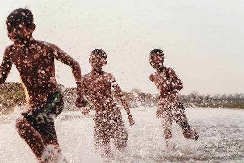 Free Three children splash energetically in a river, capturing the essence of joyful summer play. Stock Photo
