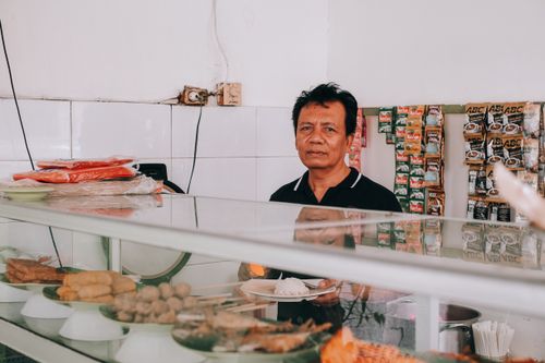 Free Chef stands behind a counter at a traditional Indonesian food stall, showcasing local snacks. Stock Photo